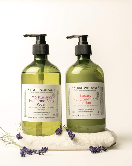 Two pump bottles of CL&RE Wellness body wash and hand and body lotion in translucent olive-green bottles, displayed on a white towel with lavender sprigs against a warm off-white background.