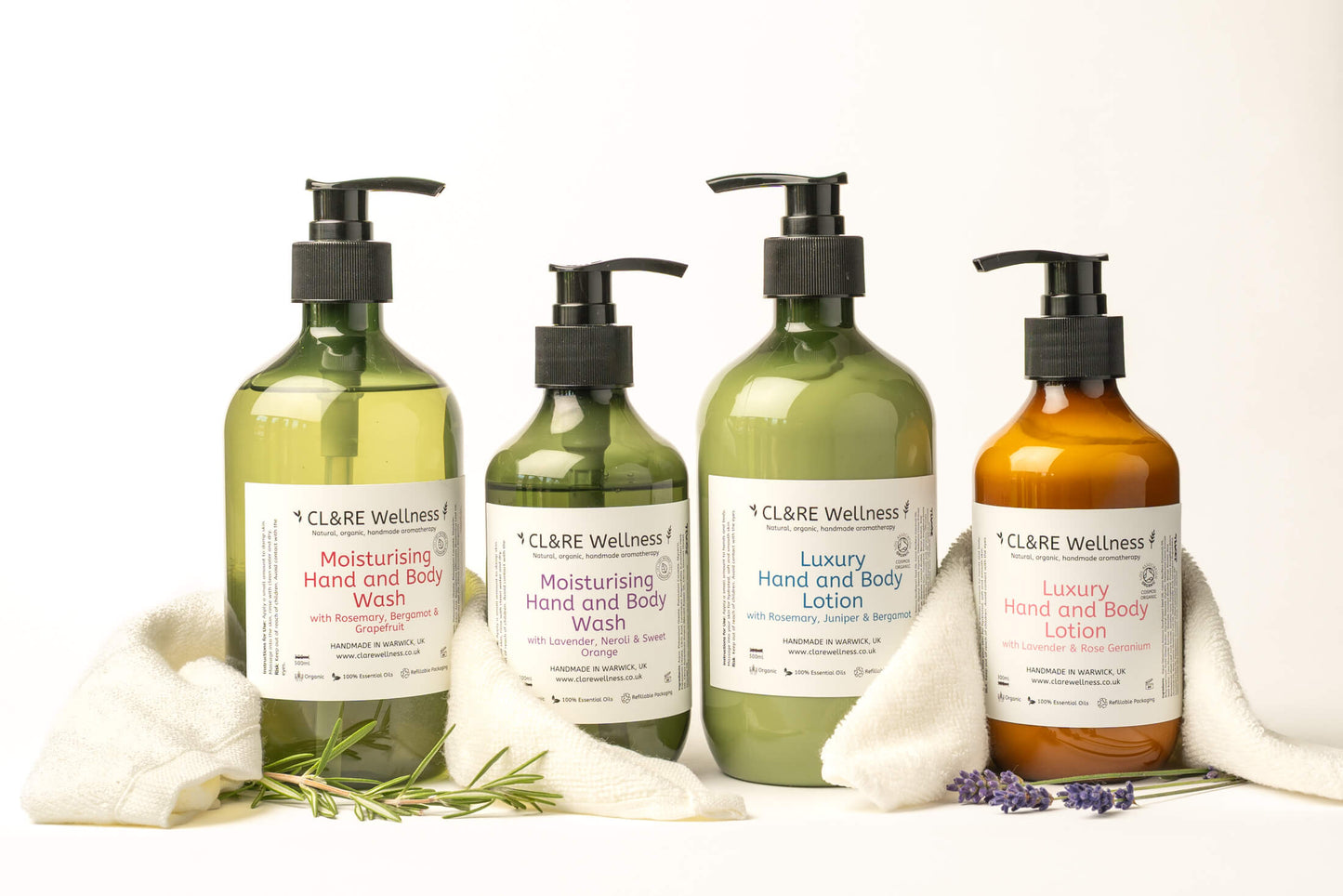 3 green and 1 amber 300ml bottles containing CL&RE Wellness Hand & Body Wash and Hand  Body Lotion surrounded by white wash cloths and some rosemary and lavender.