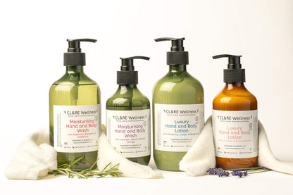 3 green and 1 amber 300ml bottles containing CL&RE Wellness Hand & Body Wash and Hand  Body Lotion surrounded by white wash cloths and some rosemary and lavender.