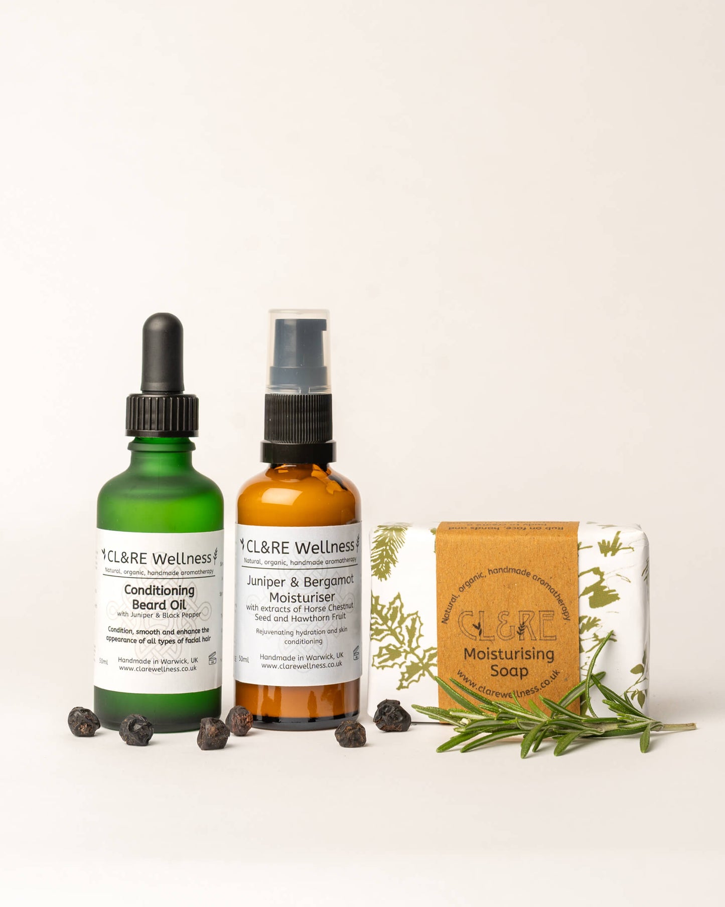 CL&RE Wellness skincare products including a Conditioning Beard Oil bottle, a soap bar, and a Facial Moisturiser bottle on a white background with fresh rosemary sprigs and juniper berries.