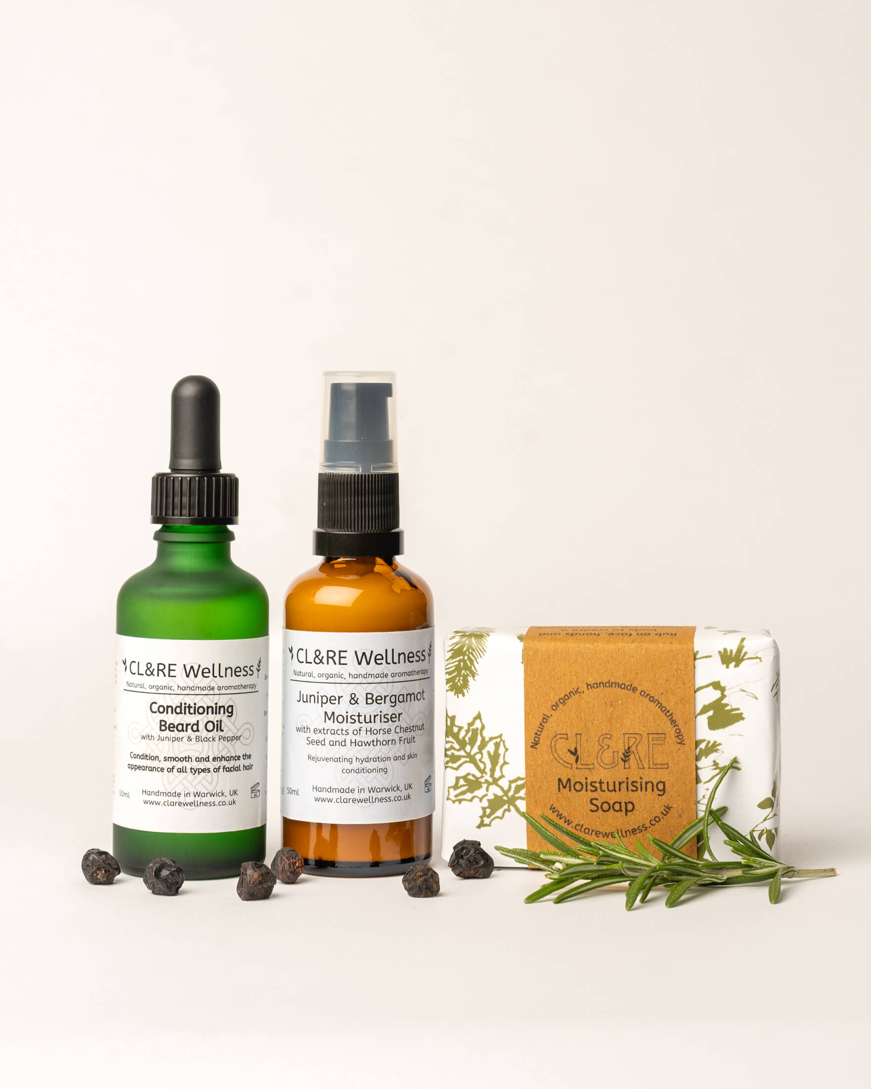 CL&RE Wellness skincare products including a Conditioning Beard Oil bottle, a soap bar, and a Facial Moisturiser bottle on a white background with fresh rosemary sprigs and juniper berries.