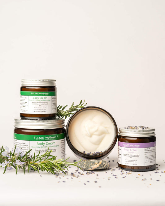 Collection of four CL&RE Wellness body cream jars with lavender flowers and rosemary sprigs on a white background