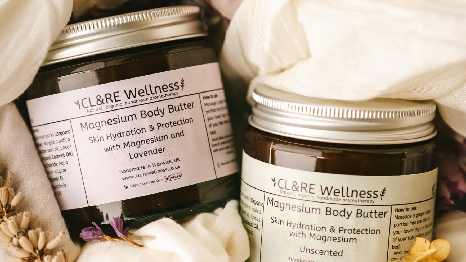 Two jars of CL&RE Wellness Magnesium Body Butter surrounded by flowers and fabric.