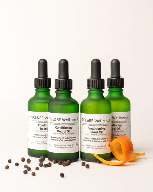 Four green bottles of CL&RE Wellness Conditioning Beard Oil on a white background with an orange peel and peppercorns.