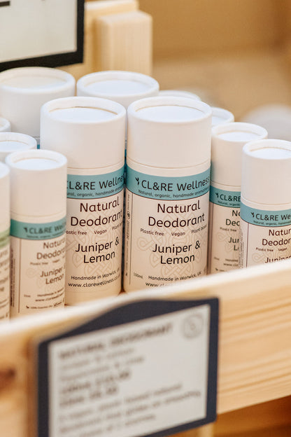 A row of natural deodorants in white cardboard tubes with CL&RE Wellness branded label saying Natural Deodorant Juniper & Lemon, Plastic-free, Vegan and Plant Based, in a wooden rack.