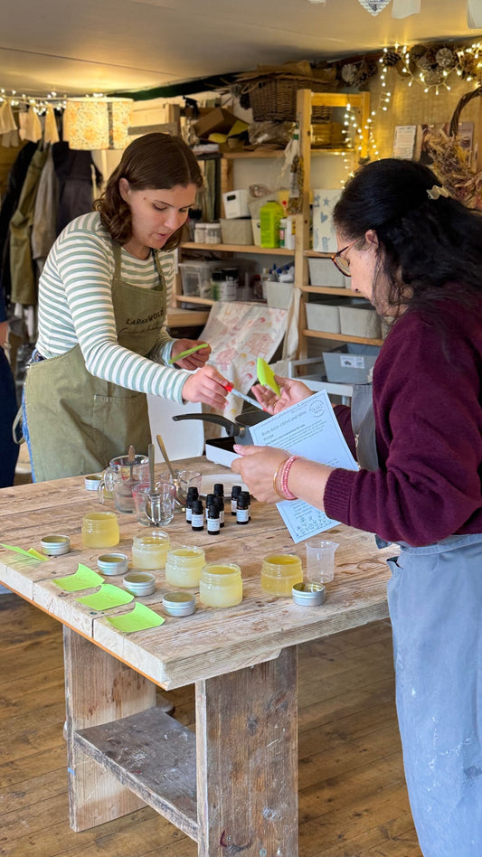 Two women in a workshop setting with various items on a table.