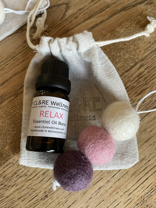 Bottle of CL&RE Wellness Relax Essential Oil blend with a purple colored natural wool felt diffuser and a linen bag, on a wooden table.